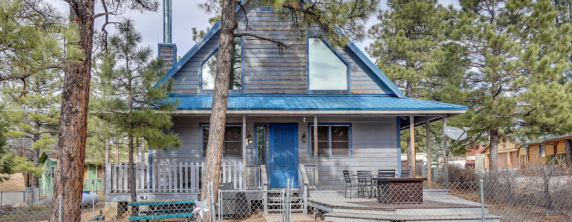 A rustic blue cabin in the woods with a chimney and front porch.